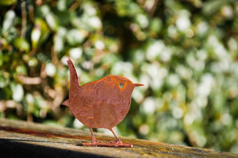 Side view of weathered steel wren fence topper captured atop a log edge, emphasising its graceful beak, tail and cut-out details. This artisan rusty metal bird décor is designed to embrace the elements and develop a unique patina over time. Ideal for cottage gardens, pergolas and porch displays; a tasteful nod to beloved British garden birds and nature-led design.
