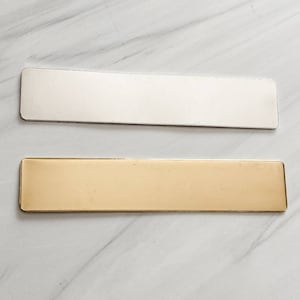 May include: Two rectangular metal nameplates, one silver and one gold. The nameplates are blank and ready to be engraved.
