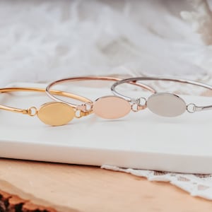 May include: Three oval-shaped bangle bracelets with a smooth, polished finish. The bracelets are in gold, rose gold, and silver.