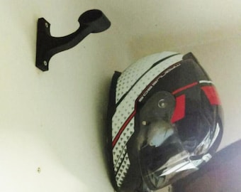 Può includere: Un portacasco nero montato su una parete bianca con un casco da moto nero e bianco con accenti rossi appeso ad esso.