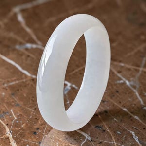 Pode incluir: Um bracelete rígido branco sólido, liso e com acabamento polido e brilhante. O acessório circular apresenta um perfil exterior arredondado e uma espessura consistente, exibindo uma aparência limpa e opaca com reflexos de luz subtis.