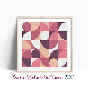 Può includere: Un modello di punto croce digitale con un design geometrico con cerchi e semicerchi rosa, pesca, bianco e viola. Il modello è incorniciato in una cornice di legno chiaro. "Cross Stitch Pattern PDF" è scritto sotto la cornice.