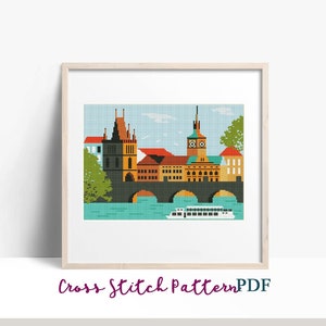 May include: A cross stitch pattern of a colorful cityscape with a bridge and a boat. The buildings are in a variety of colors, including red, yellow, orange, and green. The bridge is brown and has arches. The boat is white and has a blue stripe. The pattern is in a frame and has the text "Cross Stitch Pattern PDF" below it.