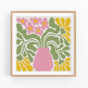 Puede incluir: Un patrón de punto de cruz de un jarrón rosa con hojas verdes y flores amarillas. El jarrón está en el centro del diseño, rodeado de hojas y flores.