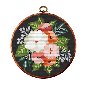 May include: A round cross-stitch floral design featuring a bouquet of flowers in shades of white, pink, and orange, set against a black background. The embroidery is framed in a wooden hoop with a bronze-colored hanging loop.