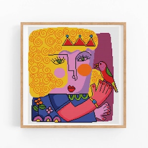 Könnte beinhalten: Gerahmtes Kreuzstich-Kunstwerk mit einem stilisierten Porträt. Die Person hat gelocktes Haar, eine Krone und rosa Haut. Ein roter und grüner Vogel sitzt auf ihrer Hand. Die Person trägt ein blaues Oberteil.