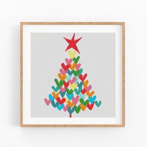 May include: A square framed cross-stitch pattern featuring a Christmas tree shape constructed from small, multi-colored hearts in shades of red, pink, yellow, green, and blue. A large red star sits at the top of the tree, all set against a white grid.