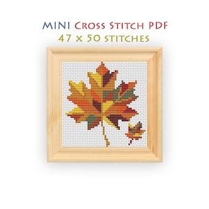 May include: A mini cross stitch PDF pattern featuring a large maple leaf and a smaller leaf in shades of yellow, orange, red, and brown. The design is displayed in a light wood frame with the text MINI CROSS STITCH PDF 47 x 50 STITCHES above.