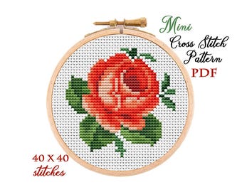 May include: A cross-stitch pattern of a red rose with green leaves, displayed in a wooden embroidery hoop. The text "Mini Cross Stitch Pattern PDF" is above the design. The text "40 x 40 stitches" is below the design.