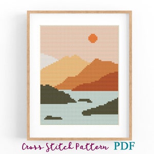 Puede incluir: Patrón de punto de cruz de un paisaje de puesta de sol con montañas, un lago y un sol en el cielo. Las montañas son de tonos naranja, marrón y amarillo. El lago es azul y verde. El sol es naranja.
