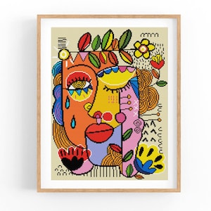 Puede incluir: Impresión artística abstracta que representa un rostro compuesto por formas y patrones geométricos. La obra de arte utiliza colores como naranja, amarillo, azul, rojo y verde, y está enmarcada en un marco de madera marrón claro.