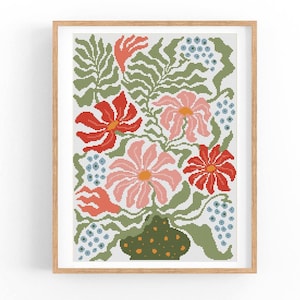 May include: A framed floral cross-stitch pattern. The design features red and pink flowers, green leaves, and blue accents, all set against a white background. The flowers are arranged in a vase with a green and brown dotted pattern. The frame is made of light brown wood.