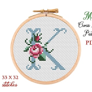 May include: A cross stitch pattern for the letter K with a blue outline and a pink rose with green leaves. The pattern is 33 stitches wide and 32 stitches high. The pattern is in a wooden embroidery hoop.