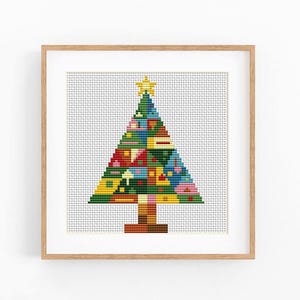 May include: A framed cross-stitch embroidery featuring a stylized Christmas tree composed of various geometric shapes in vibrant colors including red, blue, green, and yellow, topped with a yellow star, set against a white grid background.