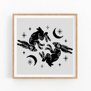 Puede incluir: Patrón de punto de cruz en blanco y negro con dos conejos estilizados en un círculo con lunas crecientes y estrellas.