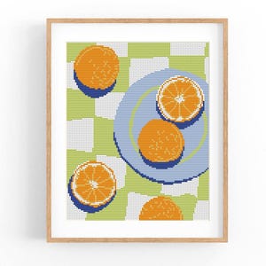 Puede incluir: Una impresión artística enmarcada con una naturaleza muerta de naranjas. La obra representa naranjas enteras y en rodajas sobre un plato azul y dispersas sobre un fondo a cuadros verde y blanco. Las naranjas son naranjas con sombras azules.