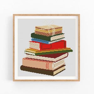 May include: A framed cross-stitch art piece featuring a stack of colorful books. The books are in various colors, including red, green, and tan, and are tied together with a white string. The artwork is set against a light gray background.