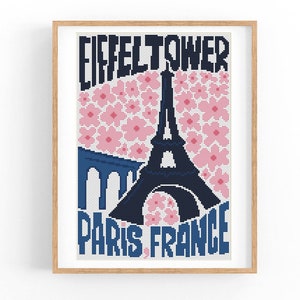 May include: Cross-stitch pattern featuring a black silhouette of the Eiffel Tower in Paris, France, with pink flower accents. The text "Eiffel Tower Paris France" is included in the design.