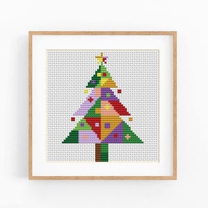 May include: A framed cross-stitch artwork featuring a stylized Christmas tree composed of geometric, multi-colored triangular and square segments in shades of green, red, yellow, purple, and pink, topped with a small yellow star, set in a light wood frame.