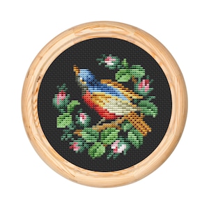 May include: A framed cross-stitch embroidery depicting a colorful bird perched on a branch with green leaves and pink flowers.