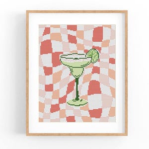 Puede incluir: Impresión enmarcada de un cóctel de margarita pixelado. La bebida verde claro con una rodaja de lima se encuentra sobre un fondo geométrico de cuadrados rojos, melocotón y blancos. La obra de arte se presenta en un marco de madera.