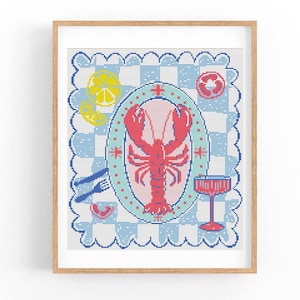 Może przedstawiać: Oprawione dzieło sztuki haftu krzyżykowego przedstawiające czerwonego homara na różowym owalnym talerzu, otoczonego plasterkami cytryny, plasterkiem pomidora i kieliszkiem do koktajli. Tło to niebiesko-biały wzór w kratę.