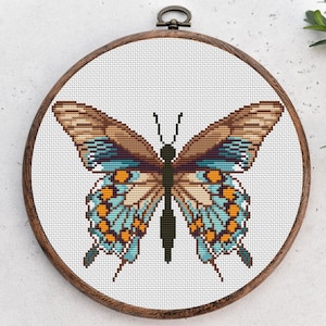 May include: A cross-stitch embroidery of a butterfly with brown, blue, and orange wings. The butterfly is framed in a wooden hoop.