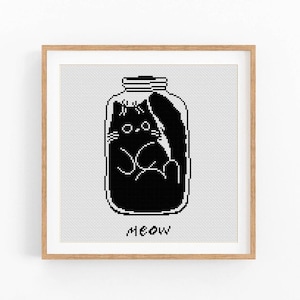 Puede incluir: Una obra de arte en punto de cruz enmarcada que representa un gato negro dentro de un tarro de cristal. El gato está estilizado con líneas y formas simples. La palabra "meow" está bordada en la parte inferior. El fondo es una cuadrícula gris claro.