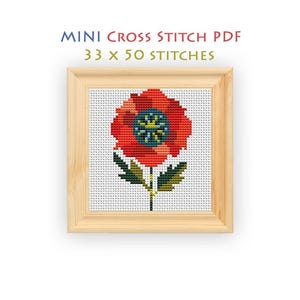 May include: A cross stitch pattern titled MINI CROSS STITCH PDF 33 x 50 STITCHES featuring a red poppy flower with a dark blue and yellow center and green leaves, displayed within a light-colored wooden frame on a white grid background.