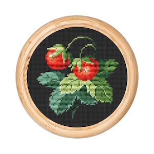 May include: A cross-stitch embroidery featuring two red strawberries and green leaves on a black backdrop, presented within a circular wooden frame. The strawberries have white highlights.