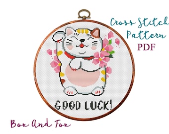 May include: Cross stitch pattern PDF of a white cat with pink and yellow accents holding a pink flower. The cat is sitting in a circle with the text "Good Luck!" below it.