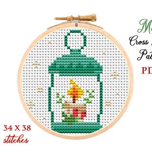 May include: A cross stitch pattern for a small lantern with a lit candle inside. The pattern is in a wooden embroidery hoop and is 34 x 38 stitches. The pattern is for a mini cross stitch project.