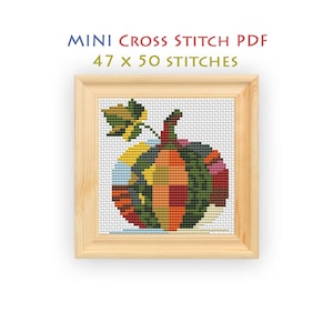 May include: A cross stitch pattern titled MINI CROSS STITCH PDF 47 x 50 STITCHES featuring a pumpkin composed of multicoloured geometric segments in shades of orange, green, yellow, and red, framed in a light-coloured wooden square frame.