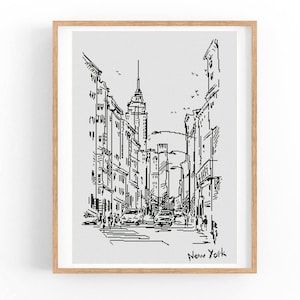 May include: A framed black and white sketch of a New York City street scene. The artwork depicts buildings, cars, and pedestrians, with the words "New York" written at the bottom. The frame is made of light-colored wood.