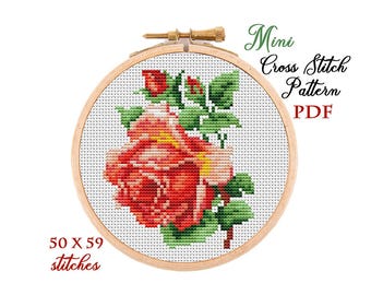 May include: A cross-stitch pattern of a red rose in a wooden embroidery hoop. The design includes green leaves and buds. Text reads "Mini Cross Stitch Pattern PDF" and "50 X 59 stitches".