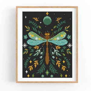 May include: Cross stitch pattern featuring a dragonfly with blue and green wings, surrounded by stylized flowers and leaves on a black background.