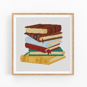 May include: A framed cross-stitch design featuring a stack of books. The books are in various colors, including brown, blue, red, and yellow, with a red bookmark. The artwork is set against a light gray background.