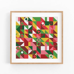 May include: A square cross-stitch pattern featuring a geometric arrangement of triangles and circles in red, green, yellow, pink, and white. The design is enclosed within a light-colored wooden frame, displaying a repeating grid of colorful shapes.