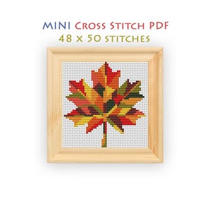 Puede incluir: Un patrón de punto de cruz de una hoja de arce en rojo, naranja, amarillo y verde, enmarcado en madera clara. El texto dice MINI CROSS STITCH PDF 48 x 50 STITCHES. El diseño presenta una cuadrícula de cuadrados de colores que representan puntos.