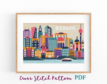 May include: A framed cross-stitch pattern of the Berlin skyline, featuring colorful buildings in shades of purple, blue, orange, and pink. The word "BERLIN" is stitched across the top. The text "Cross Stitch Pattern PDF" is at the bottom.
