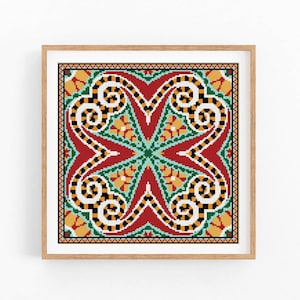 May include: A framed, square cross-stitch pattern featuring a symmetrical design. The pattern includes red, green, yellow, black, and white elements. The design has a central star shape and swirling patterns.