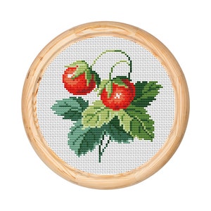 May include: A cross-stitch embroidery featuring two red strawberries with green leaves and stems, set against a white background. The artwork is framed in a round, light-coloured wooden hoop, showcasing a handcrafted, botanical theme.