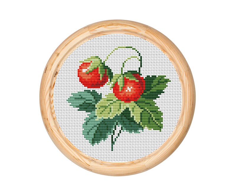 May include: A cross-stitch embroidery featuring two red strawberries with green leaves and stems, set against a white background. The artwork is framed in a round, light-coloured wooden hoop, showcasing a handcrafted, botanical theme.