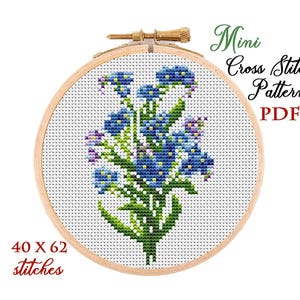 May include: A cross stitch pattern featuring a bouquet of blue flowers with green stems and leaves. The pattern is displayed in a wooden embroidery hoop and measures 40 x 62 stitches. The text "Mini Cross Stitch Pattern PDF" is displayed above the hoop.