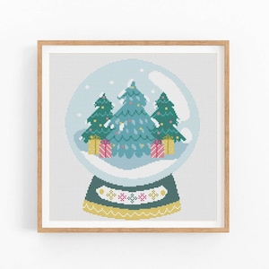 May include: A cross-stitch pattern of a snow globe with three green Christmas trees inside. The snow globe is blue and white with a gold base and a red and white patterned band.