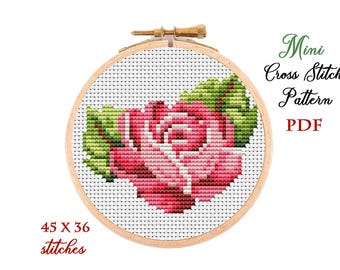 May include: A mini cross stitch pattern featuring a pink rose with green leaves. The pattern is 45 stitches wide by 36 stitches high. The pattern is displayed in a wooden embroidery hoop.