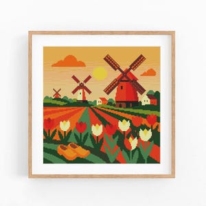 May include: A framed cross-stitch of a Dutch landscape. The scene shows red windmills, tulip fields in red, orange, and yellow, and a pair of wooden clogs. The sky is a warm orange with a yellow sun and clouds.