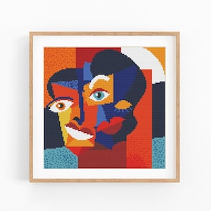 May include: A square cross-stitch embroidery featuring an abstract, multi-coloured portrait of two faces. The design uses bold blocks of red, orange, yellow, blue, and black, framed in a light-coloured wooden square frame with a white mat border.