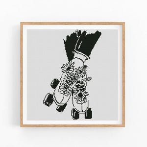 Puede incluir: Impresión artística de punto de cruz en blanco y negro de patines adornados con flores. La obra de arte está enmarcada en un marco de madera marrón claro, sobre un fondo blanco. Los patines están representados con un estilo gráfico detallado.