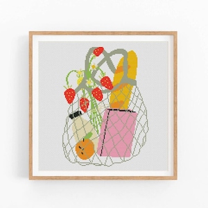 May include: A framed cross-stitch artwork depicts a mesh shopping bag filled with groceries. The bag contains a baguette, a pink paper bag, strawberries, an orange, and a small bottle. The artwork is in a square format.